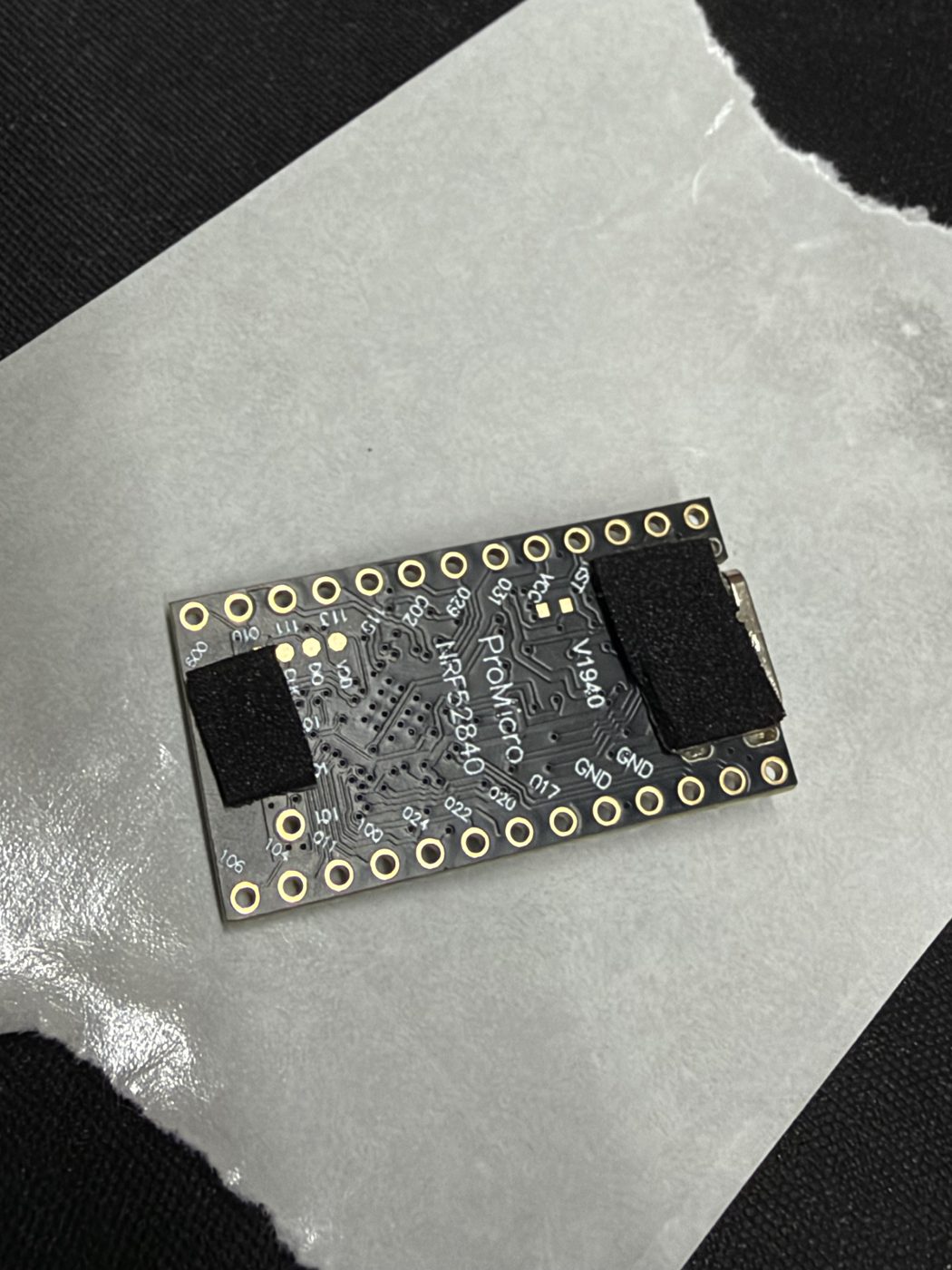 The back of the nRF52840 ProMicro board with two black foam pads applied — one across the top near the USB-C connector, one across the bottom edge.