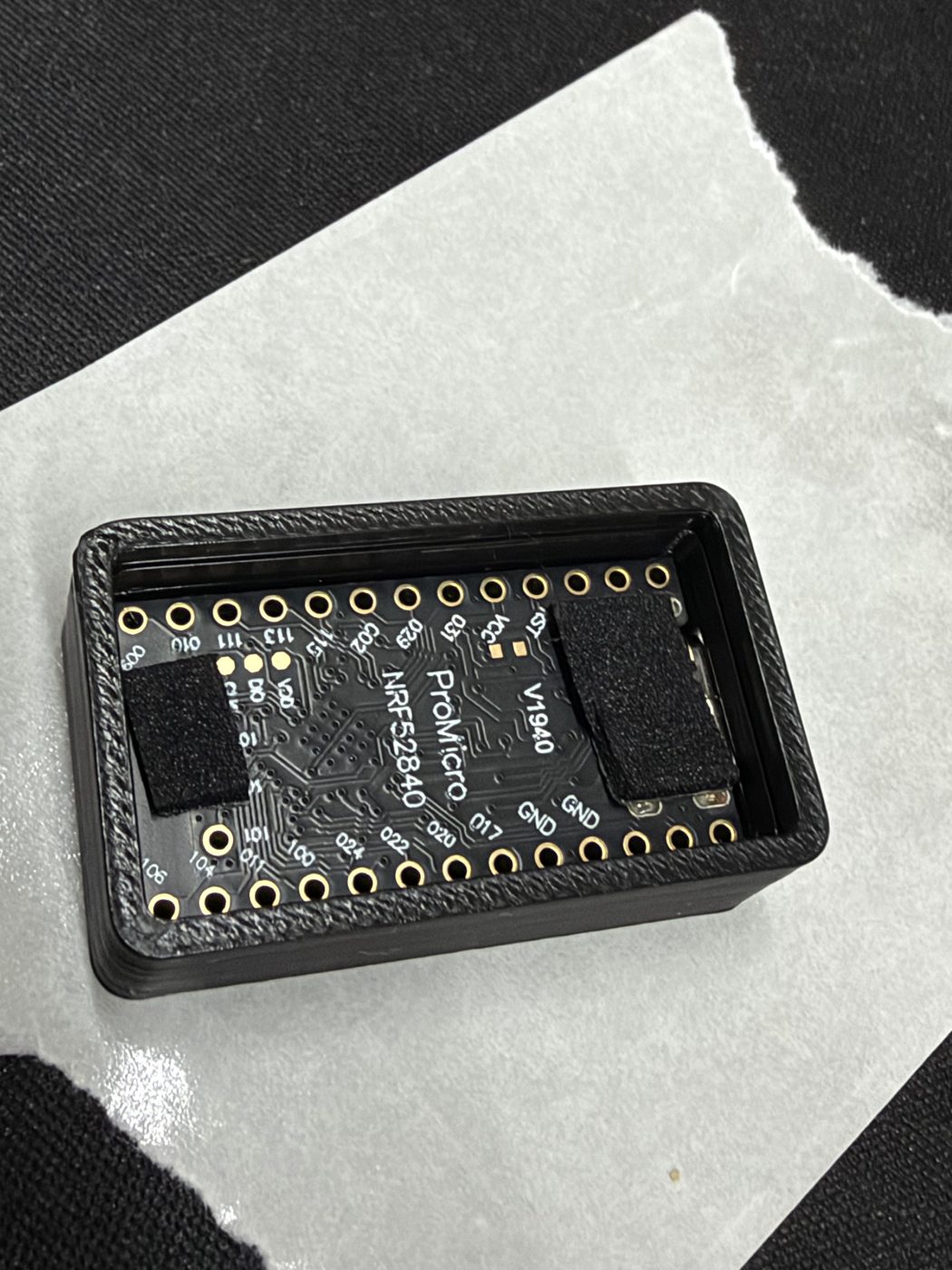 The board seated inside the black 3D-printed case base, USB-C connector aligned with the port cutout, foam pads compressed against the case walls.